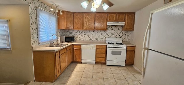 kitchen featuring under cabinet range hood, light countertops, brown cabinetry, white appliances, and a sink