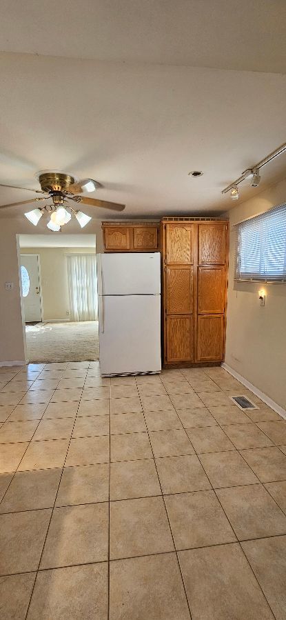 kitchen with visible vents, brown cabinets, a ceiling fan, freestanding refrigerator, and light tile patterned flooring