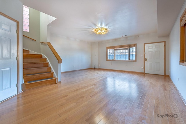 unfurnished living room featuring stairway, baseboards, and light wood-style flooring