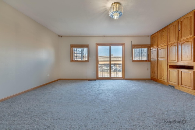 empty room featuring a notable chandelier, visible vents, light colored carpet, and baseboards