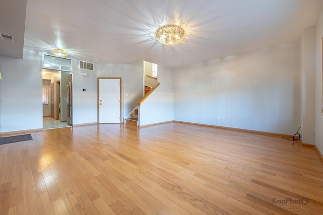 empty room featuring stairway, light wood-style floors, visible vents, and baseboards