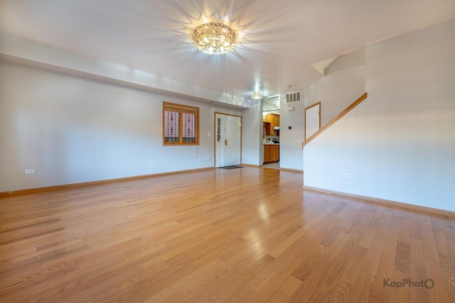 unfurnished living room with an inviting chandelier, baseboards, visible vents, and light wood finished floors