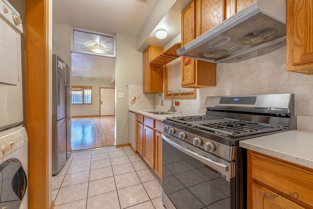 kitchen featuring light tile patterned flooring, a sink, stainless steel appliances, stacked washer / drying machine, and under cabinet range hood