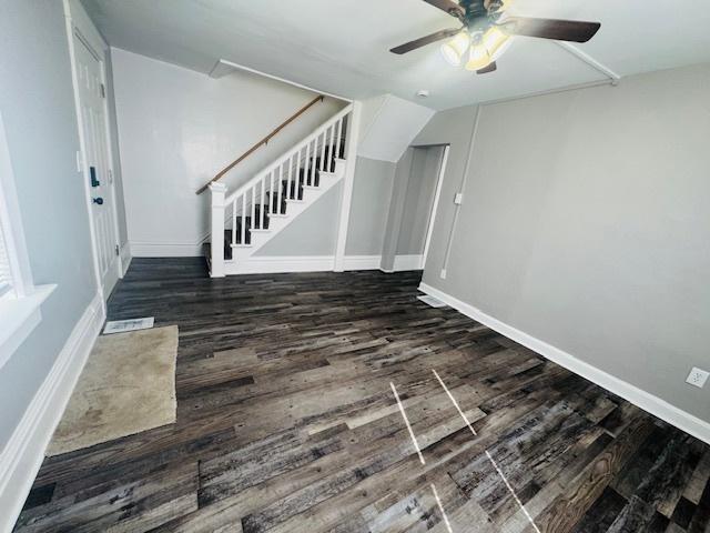 unfurnished living room featuring stairs, wood finished floors, baseboards, and ceiling fan