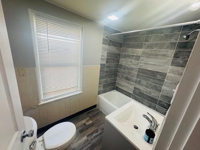 full bath with toilet, wainscoting, bathtub / shower combination, wood finished floors, and tile walls