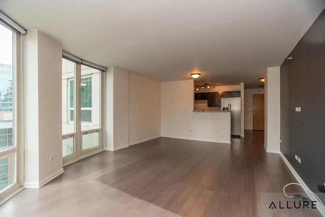 unfurnished living room with a wall of windows, baseboards, and dark wood-style floors