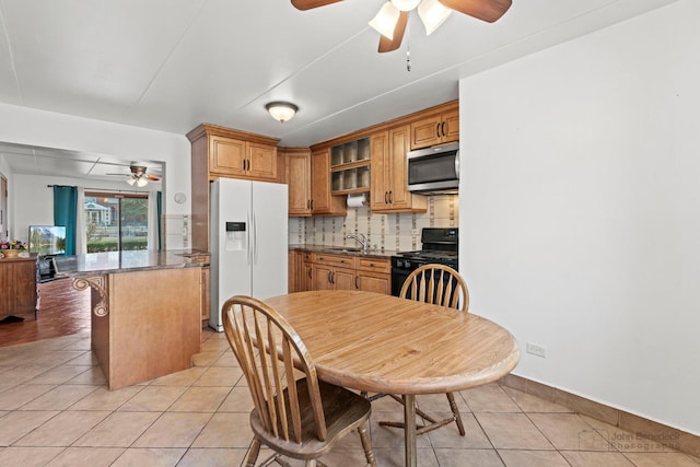 kitchen featuring light tile patterned floors, stainless steel microwave, white refrigerator with ice dispenser, and black gas stove