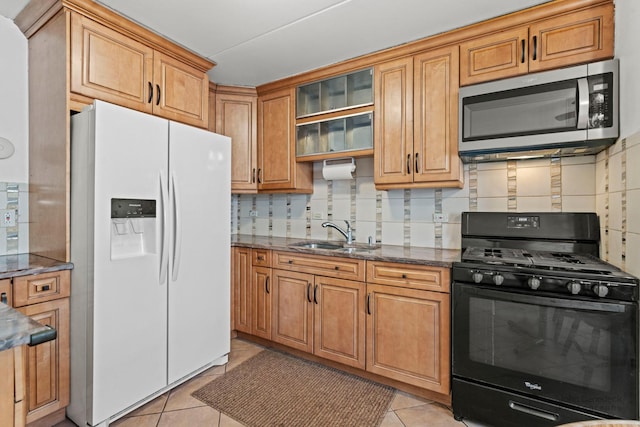 kitchen featuring dark stone countertops, black gas stove, a sink, white refrigerator with ice dispenser, and stainless steel microwave