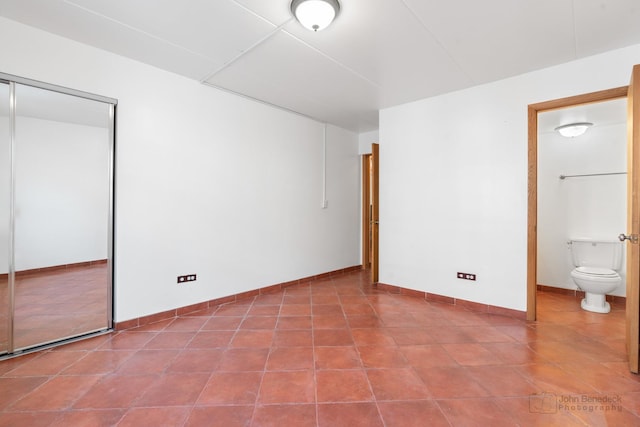 unfurnished bedroom featuring tile patterned flooring, ensuite bathroom, and baseboards