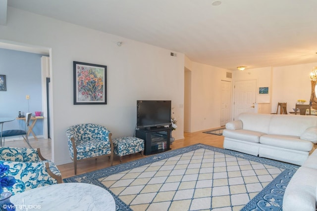 living room featuring light wood-type flooring, visible vents, baseboards, and a notable chandelier