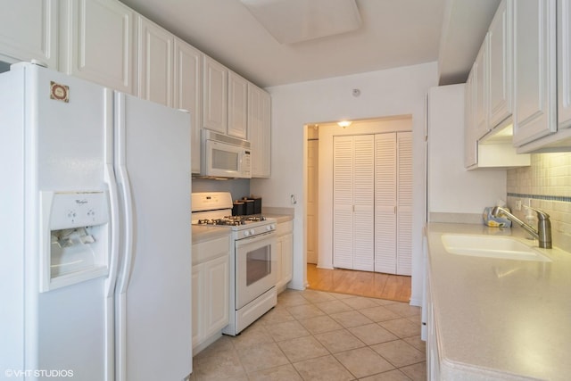 kitchen with white appliances, white cabinetry, light countertops, and a sink