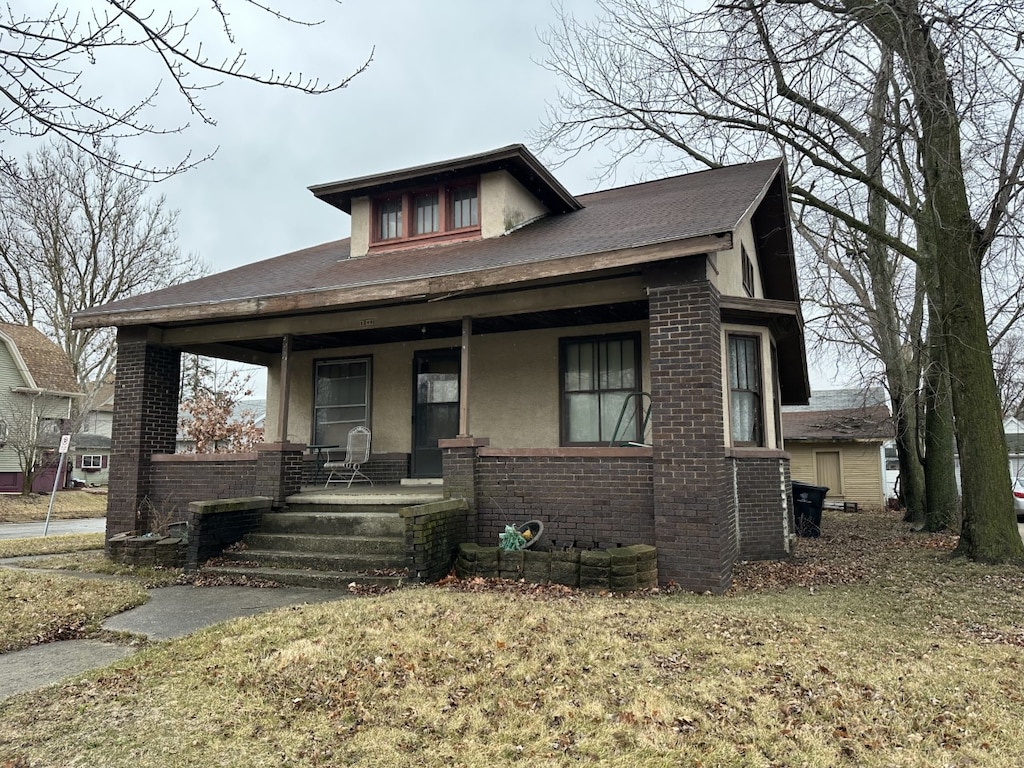 bungalow featuring stucco siding, brick siding, and covered porch