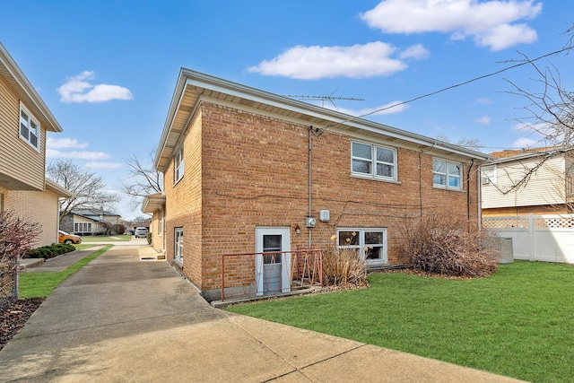 rear view of property with brick siding, a lawn, and fence