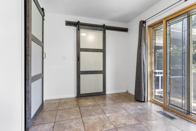 empty room featuring tile patterned flooring, visible vents, baseboards, and a barn door