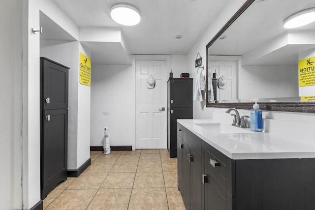 kitchen featuring baseboards, light countertops, light tile patterned floors, dark cabinetry, and a sink