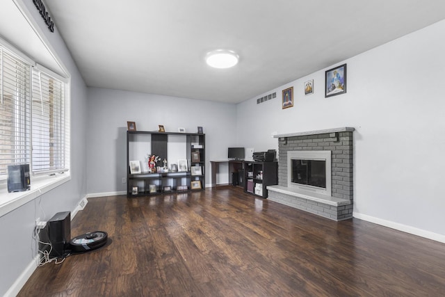 living room with visible vents, a brick fireplace, baseboards, and wood finished floors