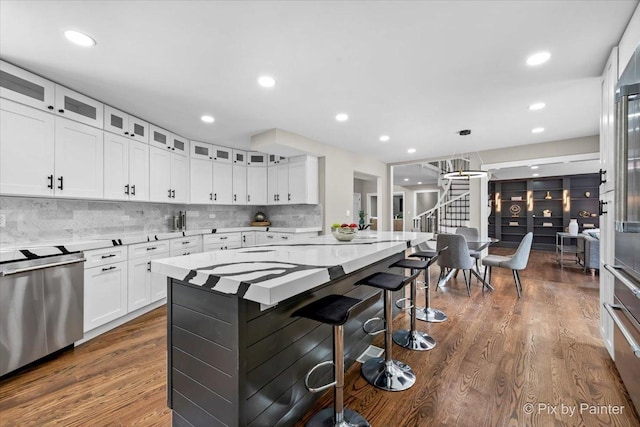 kitchen featuring tasteful backsplash, a kitchen breakfast bar, stainless steel dishwasher, white cabinets, and dark wood-style flooring