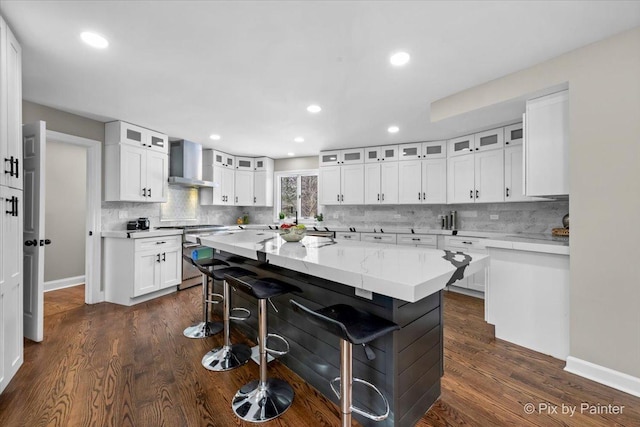 kitchen featuring a kitchen island, stainless steel range, white cabinets, a kitchen bar, and wall chimney range hood