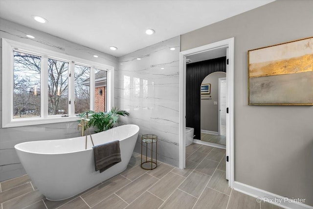 bathroom featuring recessed lighting, toilet, tile walls, and a freestanding tub