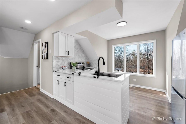 kitchen featuring tasteful backsplash, a peninsula, wood finished floors, white cabinetry, and a sink