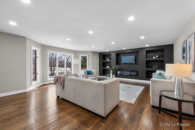 living room with built in shelves, baseboards, dark wood finished floors, recessed lighting, and a glass covered fireplace