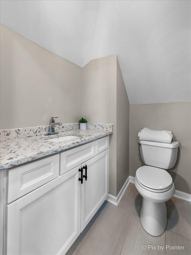 half bath featuring toilet, vanity, baseboards, and vaulted ceiling