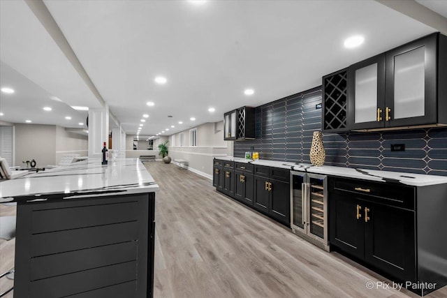 kitchen with light wood-style flooring, dark cabinetry, open floor plan, wine cooler, and light countertops