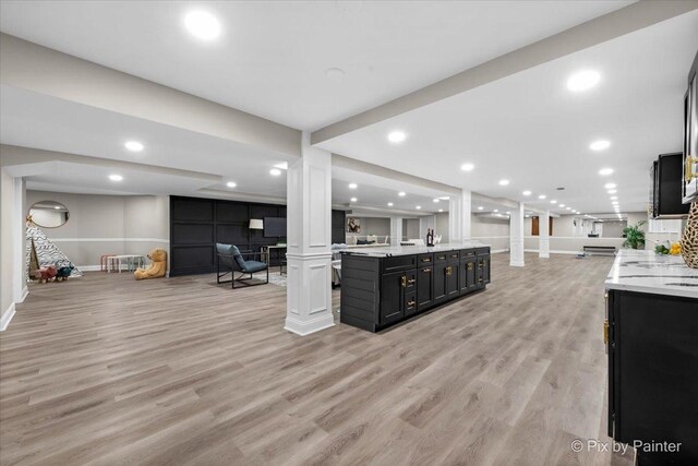 kitchen with open floor plan, light wood-type flooring, ornate columns, and dark cabinets