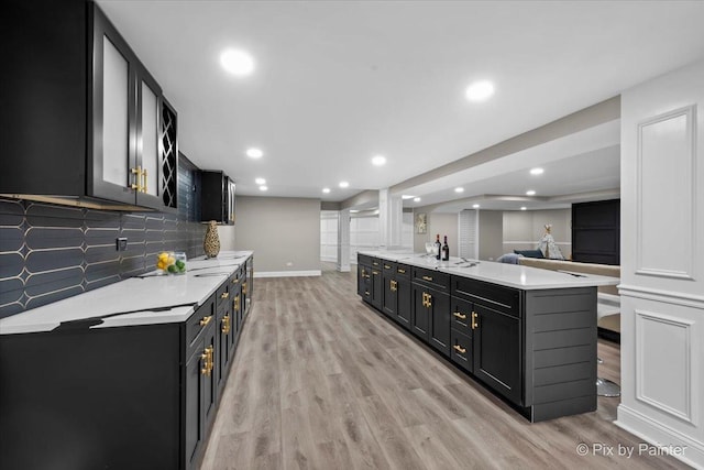 kitchen with tasteful backsplash, light wood-style floors, light countertops, baseboards, and dark cabinets