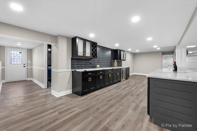 kitchen featuring baseboards, light wood-type flooring, dark cabinets, recessed lighting, and tasteful backsplash