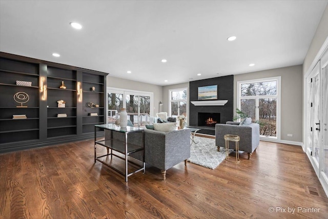 living area with a brick fireplace, plenty of natural light, and wood finished floors