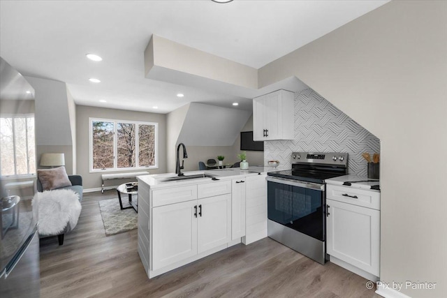 kitchen featuring open floor plan, stainless steel range with electric stovetop, a peninsula, white cabinets, and a sink