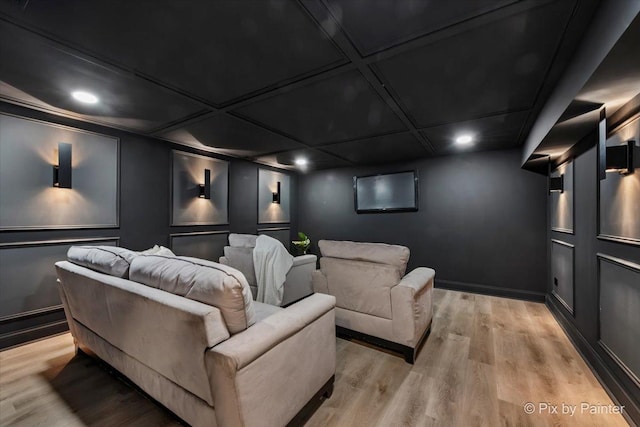 home theater room featuring a decorative wall, coffered ceiling, and light wood-type flooring