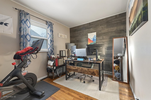 office featuring wood walls, an accent wall, baseboards, and wood finished floors