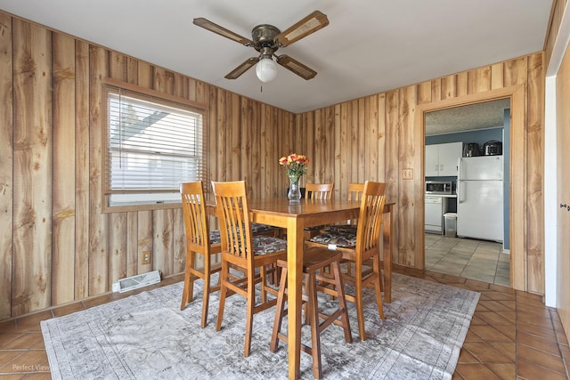 dining space with tile patterned floors, wooden walls, visible vents, and ceiling fan