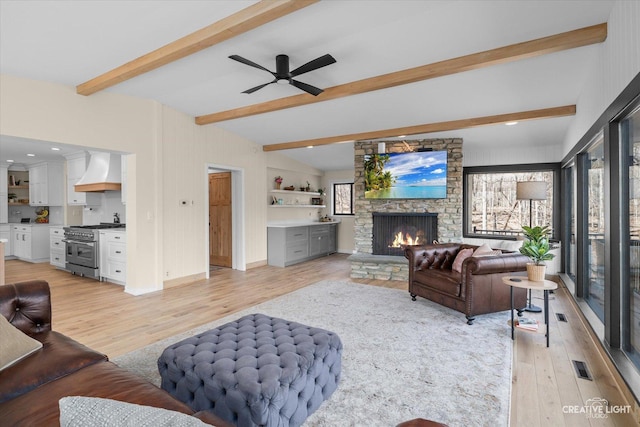 living room with visible vents, vaulted ceiling with beams, a fireplace, light wood-style floors, and a ceiling fan