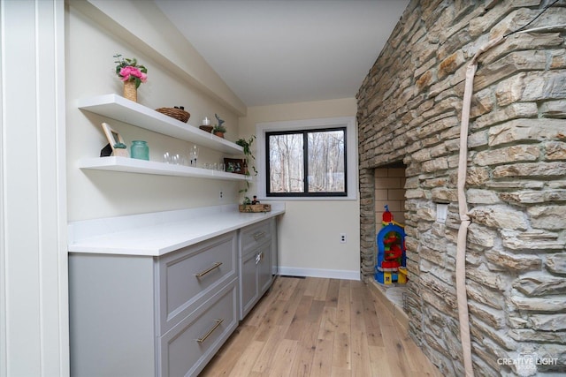 bar with baseboards, light wood-style floors, and vaulted ceiling