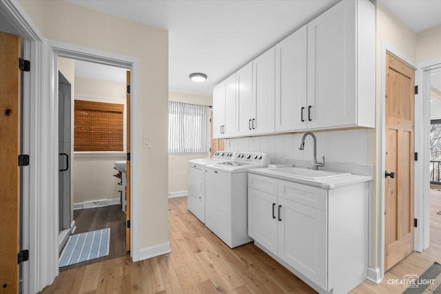 laundry room with light wood finished floors, baseboards, separate washer and dryer, cabinet space, and a sink