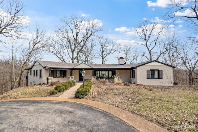 ranch-style home featuring brick siding, covered porch, and a chimney