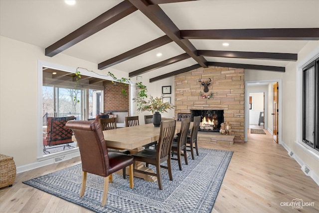 dining room with visible vents, baseboards, lofted ceiling with beams, a stone fireplace, and light wood-style floors