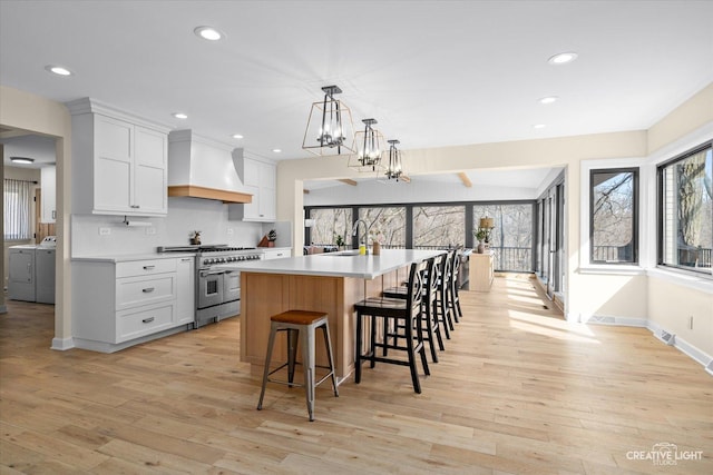 kitchen featuring custom exhaust hood, light wood-style flooring, double oven range, and washing machine and clothes dryer