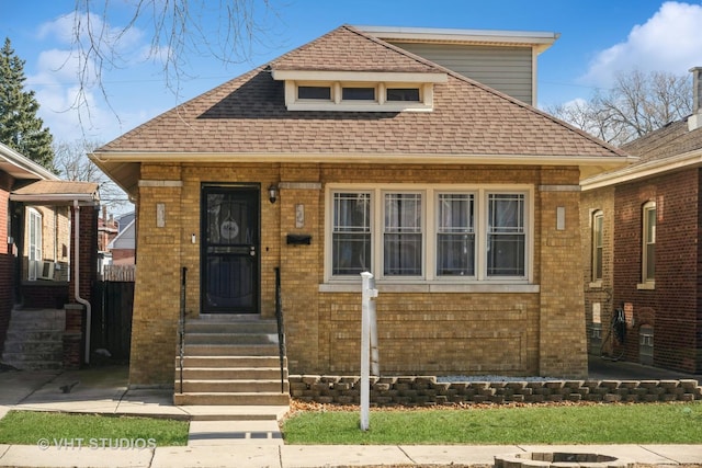 bungalow-style home featuring brick siding, entry steps, and a shingled roof