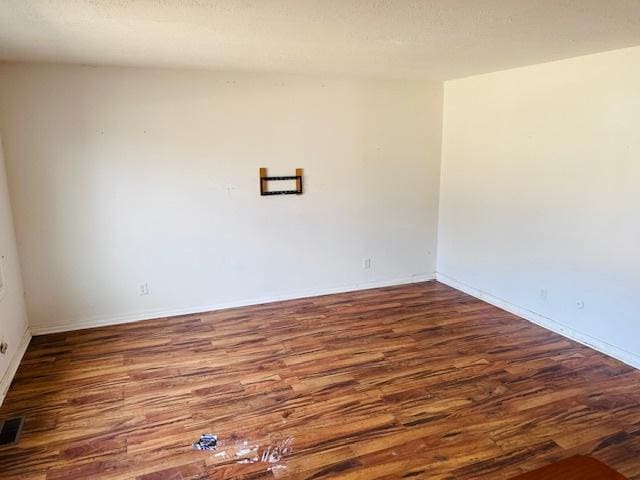 spare room featuring visible vents, a textured ceiling, baseboards, and wood finished floors