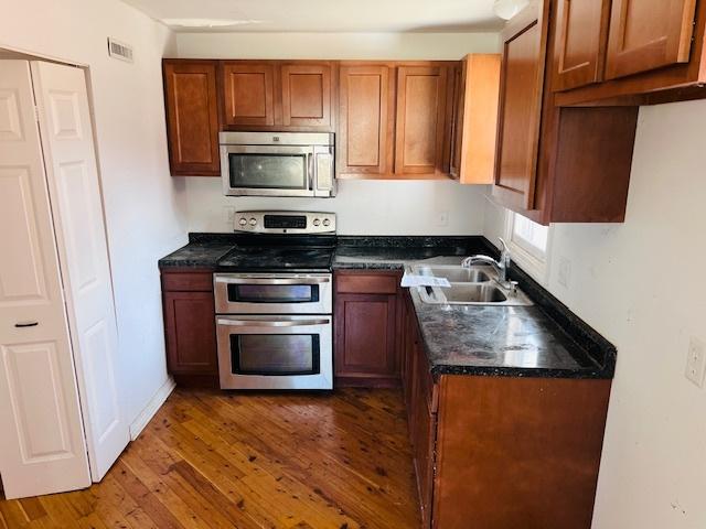 kitchen featuring dark wood-style floors, visible vents, a sink, stainless steel appliances, and brown cabinets