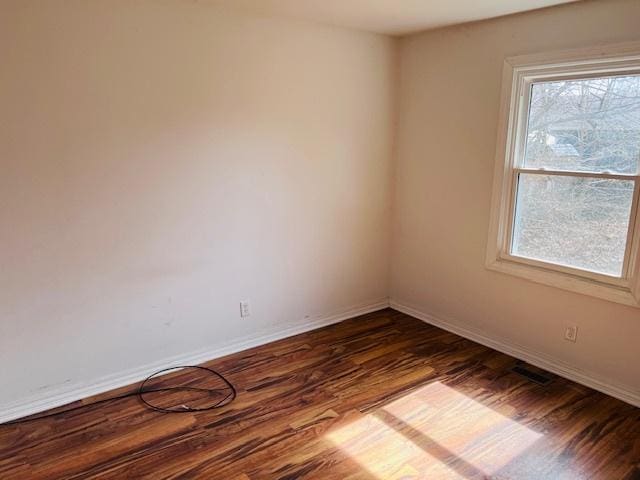 empty room with dark wood finished floors, visible vents, and baseboards