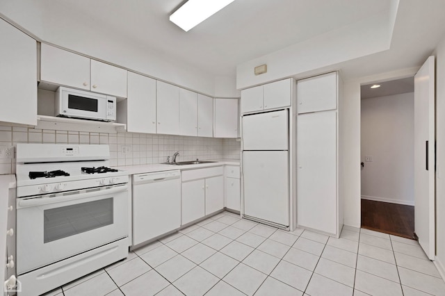 kitchen with a sink, tasteful backsplash, white appliances, white cabinets, and light countertops