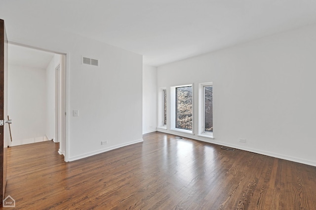 empty room featuring visible vents, baseboards, and dark wood finished floors