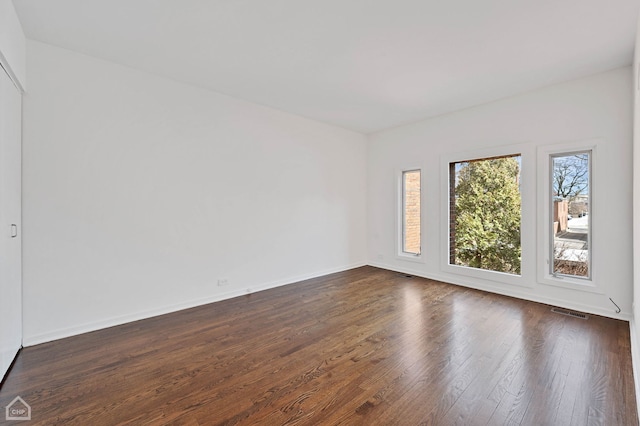 empty room featuring visible vents, baseboards, and dark wood-type flooring