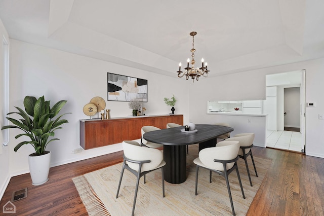 dining room with a tray ceiling, visible vents, and wood finished floors