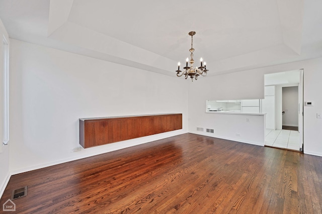 unfurnished dining area with visible vents, a raised ceiling, and hardwood / wood-style flooring